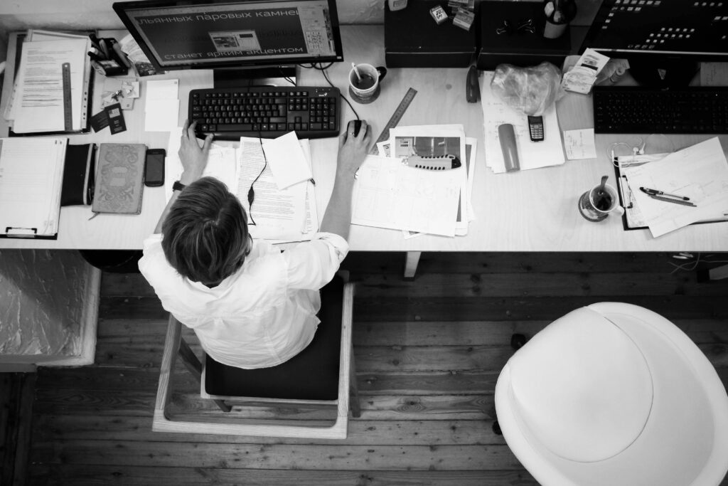 Black and white image of an employee working at a desk with papers and computer.