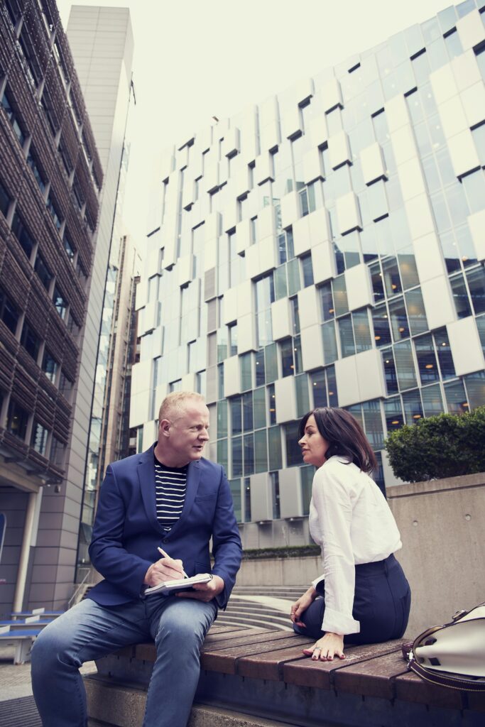 Two professionals discussing business outdoors surrounded by urban architecture.